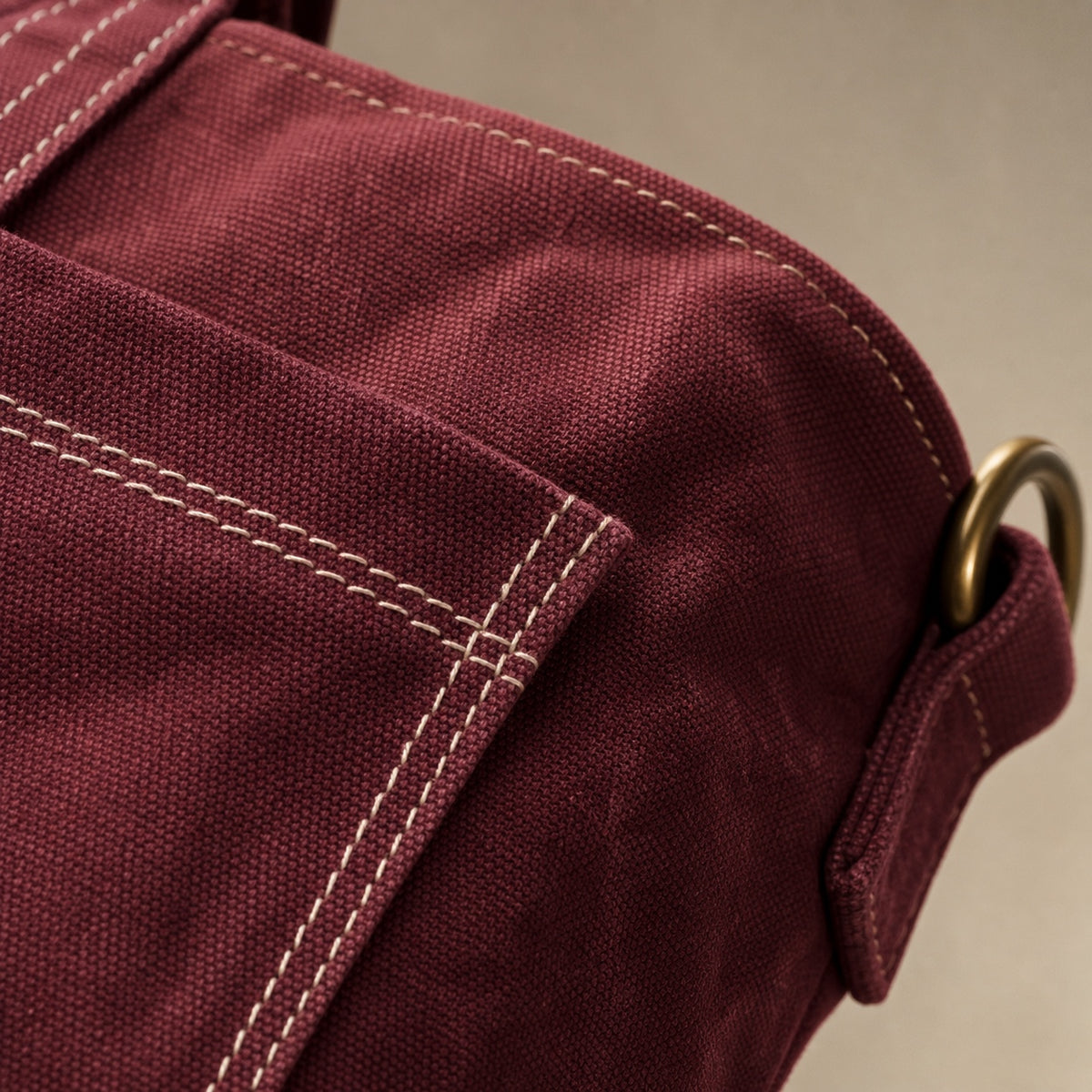 Close-up of oxblood washed canvas, contrast stitching, and antique-brass hardware