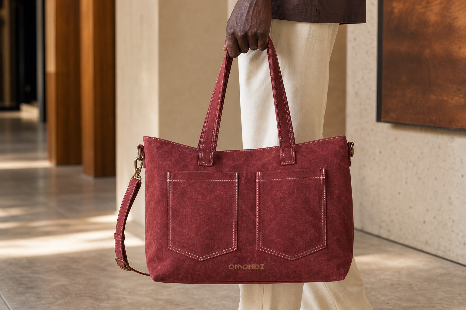 Black model carrying the oxblood OMONDI washed-canvas tote in a warm architectural interior